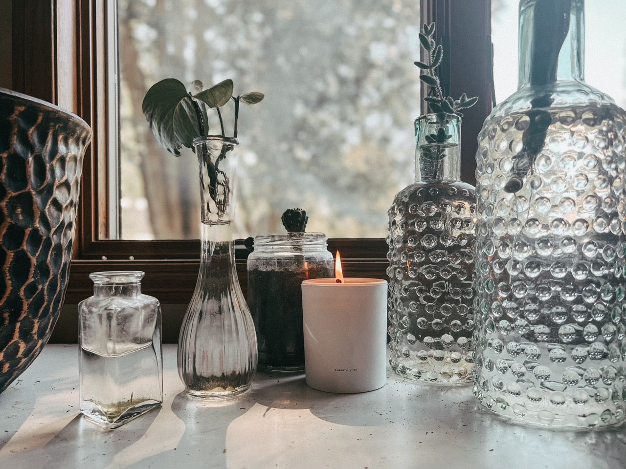 Decorative glass vases and a candle on a windowsill with a blurred outdoor background