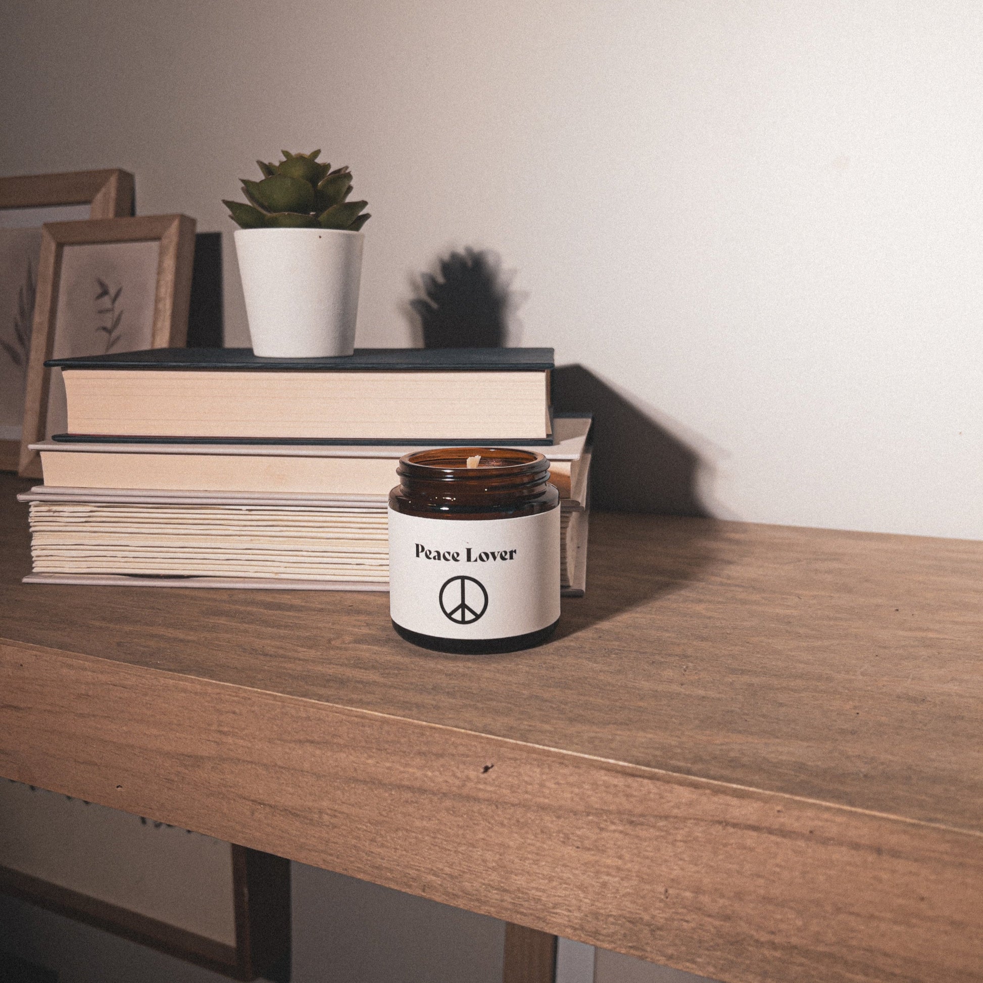 4 oz candle in amber jar with stacked books on shelf. Palo Santo & Patchouli "Peace Lover"  scented beeswax candle.
