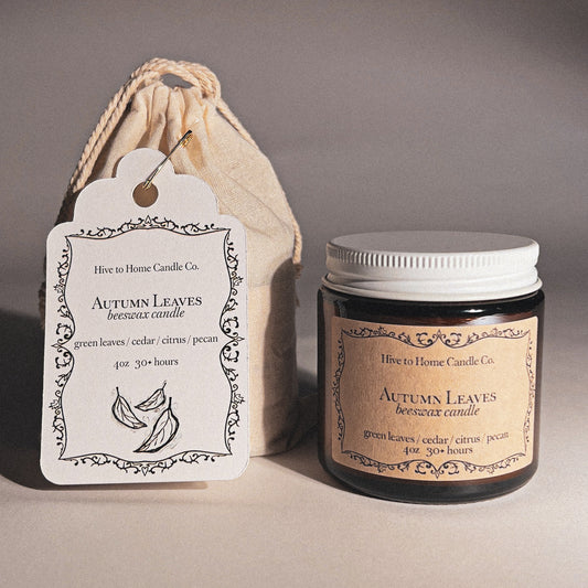 Beeswax candle labeled 'Autumn Leaves' with a matching label and drawstring bag on a neutral background.